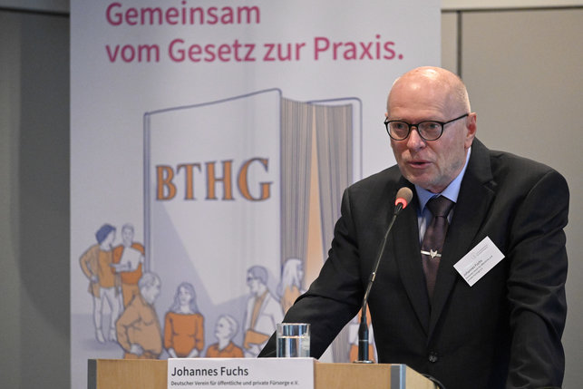 Das Foto zeigt Johannes Fuchs, Präsident des Deutschen Vereins für öffentliche und private Fürsorge e.V., hinter dem Rednerpult auf der Bühne.