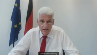 Screenshot von Dr. Rolf Schmachtenberg, Staatssekretär im BMAS, während seines Vortrags. Der Bildausschnitt zeigt ihn mit Gesicht und Oberkörper.