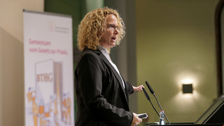 Das Bild zeigt Dr. Uda Bastians, Referentin beim Deutschen Städtetag, auf der Bühne hinter dem Rednerpult.