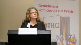 Das Bild zeigt Antje Welke, Justiziarin und Leiterin der Abteilung Konzepte und Recht der Bundesvereinigung Lebenshilfe e.V., hinter dem Rednerpult auf der Bühne.