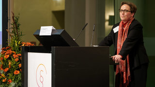 Das Bild zeigt Dr. Elisabeth Fix, Referentin beim Deutschen Caritasverband, hinter dem Rednerpult auf der Bühne.