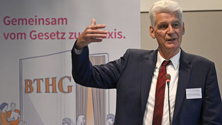 Das Bild zeigt Dr. Rolf Schmachtenberg, Staatssekretär im Bundesministerium für Arbeit und Soziales, hinter dem Rednerpult während seines Vortrags.